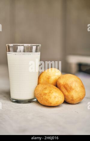 Un verre transparent avec du lait de pomme de terre sur la table à côté des tubercules de pomme de terre. Banque D'Images