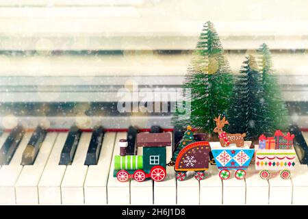 Train en bois avec arbre de Noël, cadeaux et cerfs sur fond de trois arbres de Noël manèges sur les clés de piano.Nouvel an ou fond musical de Noël avec bokeh et neige.Mise au point douce Banque D'Images