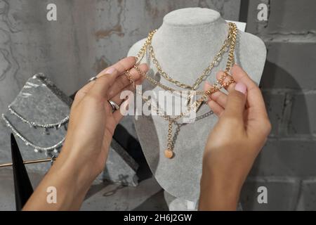 Mains de jeune femme consommateur tenant collier or sur mannequin tout en choisissant des bijoux dans luxueuse boutique Banque D'Images