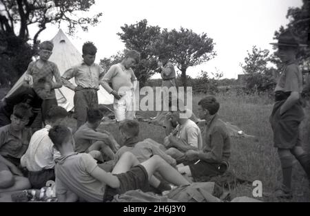 1938, historique, un camp de scouts, à l'extérieur dans un champ, un groupe de scouts de cub écoutant un garçon plus âgé jouant un ukulele, Felbridge, Surrey, Angleterre, Royaume-Uni.Le Scoutisme a commencé en 1908, après que l'officier de l'armée britannique Robert Baden-Powell ait tenu un camp expérimental sur l'île Brownsea, dans le port de Poole, l'été précédent.Environ 20 garçons ont assisté à l'événement et ont reçu une formation sur toute une gamme de compétences en plein air, y compris le suivi, la lutte contre les conflits, la fabrication d'abris à partir de branches, le nouage, la cuisine, la santé et l'assainissement, le sauvetage et les premiers soins.Le célèbre livre de Baden-Powell, « Scouting for Boys », a été publié pour la première fois en 1908. Banque D'Images