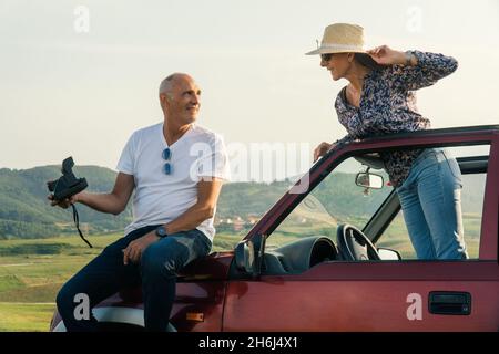 Couple âgé prenant une photo polaride et voyageant à travers la côte dans leur voiture décapotable 4x4 Banque D'Images