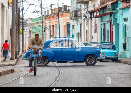 Un cubain à vélo tandis qu'une voiture de collection roule en arrière-plan, Camaguey, Cuba Banque D'Images