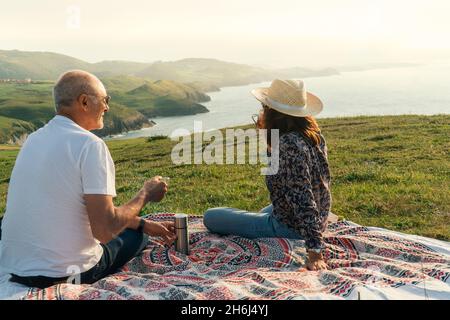 Couple âgé appréciant le coucher du soleil et prenant une tasse de thé chaud sur le rivage Banque D'Images