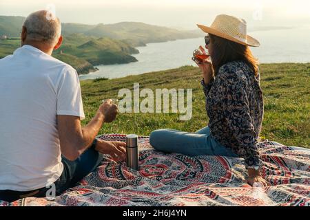 Couple âgé appréciant le coucher du soleil et prenant une tasse de thé chaud sur le rivage Banque D'Images