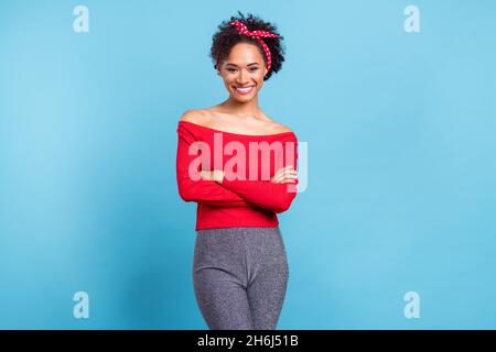 Photo de charmante femme africaine vêtue rouge off-épaules chemise souriante bras repliés isolé couleur bleu arrière-plan Banque D'Images