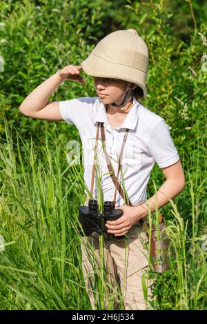 La préadolescente portant un casque en liège se tient dans les pairs de l'herbe dans la distance tenant sa main à ses yeux.Concept de découverte Banque D'Images