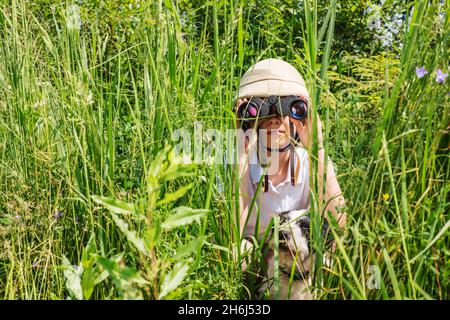 Préadolescence fille portant un casque de liège se cachant dans l'herbe avec son chien regardant à travers des jumelles Banque D'Images