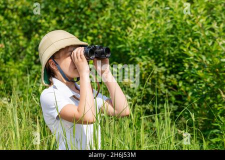 Préadolescence fille portant un casque de liège debout dans l'herbe regardant à travers des jumelles.Concept de découverte Banque D'Images