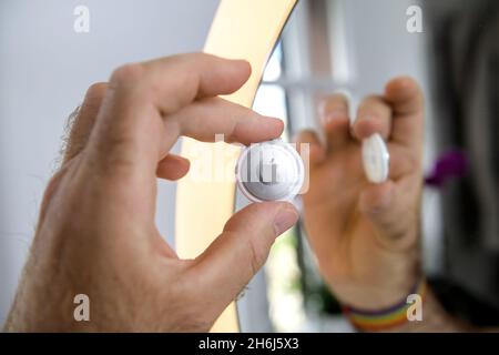 Homme de la main de hissant le nouveau dispositif de suivi AIRTAG d'Apple Computers reflété dans le miroir Banque D'Images