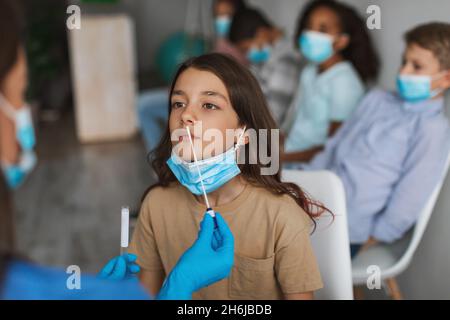 Fille se faisant tester pour le coronavirus assis avec le groupe d'enfants à l'intérieur Banque D'Images