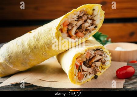 Rouleau classique de shawarma avec poulet et légumes dans du pain pita sur fond de bois foncé avec tomates cerises et persil vert Banque D'Images