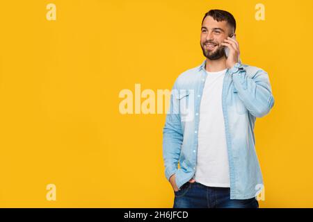 Joyeux homme européen adulte avec barbe parle par téléphone, isolé sur fond jaune Banque D'Images