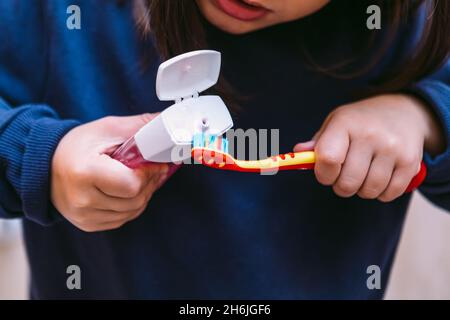 Détail de brosse à dents verser le dentifrice par petite fille dans un sweat-shirt bleu foncé, dans la salle de bains.Concept de brossage des dents, d'hygiène et d'enfance. Banque D'Images