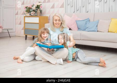 Une maman caucasienne souriante enseignant des filles assises sur le sol dans le salon.Concept de famille heureux. Banque D'Images