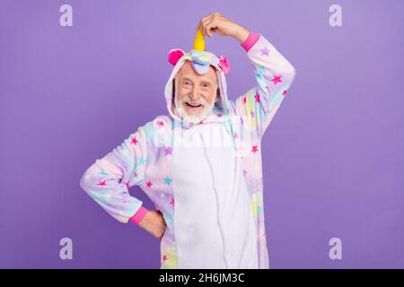 Photo de l'homme funky impressionné pensioner unicorn vêtements de nuit main corne sourire isolé couleur violet fond Banque D'Images