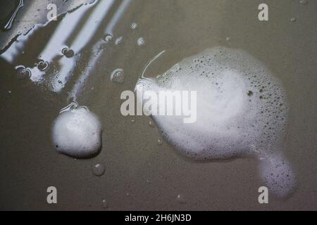 Gros plan de la mousse de savon avec bulles à travers le dessus de la cuisine, pendant le lavage de vaisselle, avec réflexion de la lumière de fenêtre. Banque D'Images