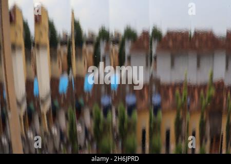 Vue abstraite vue à travers une fenêtre en verre nervuré, montrant un paysage fragmenté non défini avec des maisons et des arbres. Banque D'Images