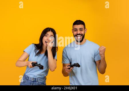 Émotions de la victoire et de la perte dans le jeu en ligne.Joueur arabe gars se réjouir du succès près de la femme bouleversée, fond jaune Banque D'Images