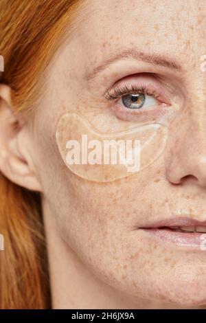 Portrait demi-visage de belle femme aux cheveux rouges avec des taches de rousseur appréciant le soin de la peau à l'aide de timbres hydratants Banque D'Images