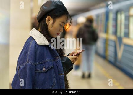 Addicted de téléphone fille chinoise ne payer aucune attention sur l'arrivée train sur plate-forme défilement des médias sociaux Banque D'Images