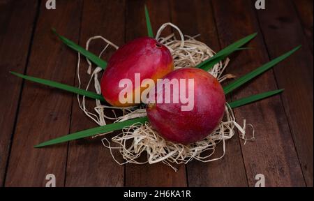 fruits mangues avec feuilles sur paille et table en bois Banque D'Images