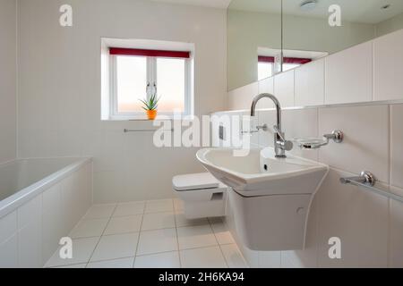 Essex, Angleterre - novembre 18 2019 : salle de bains entièrement carrelée blanche avec lavabo mural en céramique, baignoire et toilettes Banque D'Images