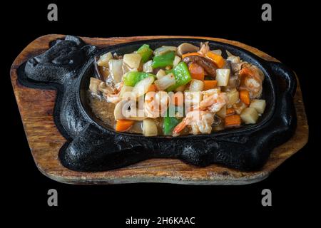 Un plat traditionnel japonais dans une poêle en fonte, crevettes frites avec des légumes.Sur fond noir, gros plan. Banque D'Images