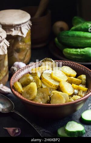 Salade de concombre marinée dans un bol et bocaux sur fond noir Banque D'Images