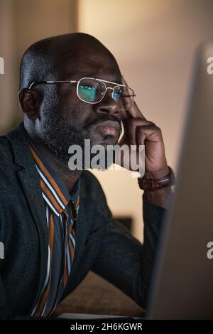 Gros plan sur un homme d'affaires africain pensif en lunettes regardant un moniteur d'ordinateur et travaillant en ligne Banque D'Images