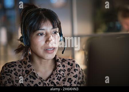 Agent de centre d'appels féminin et convivial avec micro-casque/oreillette travaillant sur la ligne d'assistance au bureau Banque D'Images