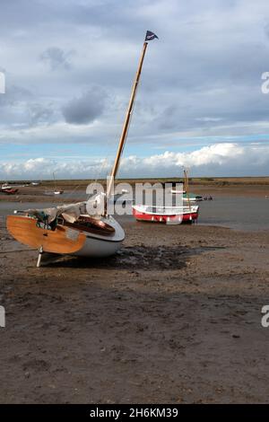 Petit bateau à voile traditionnel avec voiles sur le boum siting sur la boue à marée basse la rivière Burn à Burnham Overy North Norfolk Angleterre Banque D'Images