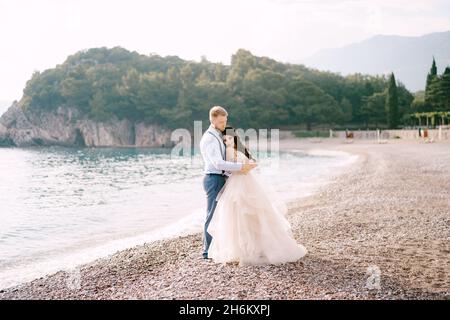 La mariée et le marié se tiennent sur le rivage et le hug de galets, le marié épouse les épaules de la mariée Banque D'Images