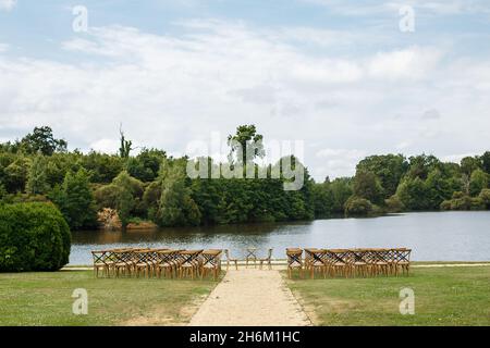 Cérémonie de mariage sur le fond du lac.Rangées de chaises en bois pour les clients debout sur l'herbe dans le jardin du château de France. Banque D'Images