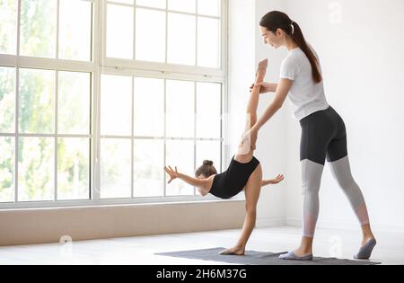 Coach aidant la petite fille à faire de la gymnastique en salle de gym Banque D'Images