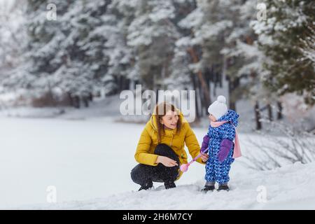 Une jeune femme sculpte des boules de neige avec sa petite fille dans la forêt d'hiver.Mignon enfant dans des vêtements chauds ayant amusement extérieur avec la mère.Maman et fille.Famil Banque D'Images