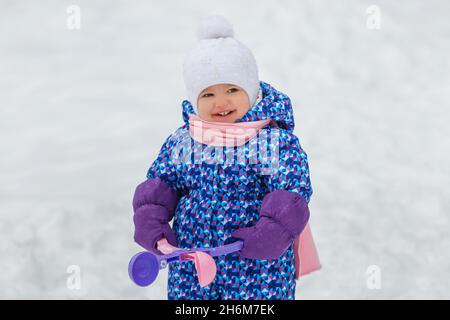 Mignon enfant de deux ans jouant avec le jouet de fabrication de boules de neige.Petite fille souriante s'amusant dans le parc d'hiver.Concept de soins et de vêtements chauds Banque D'Images