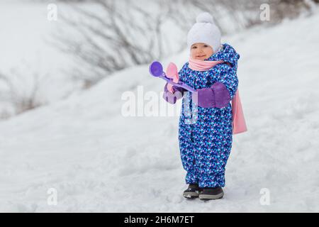 Mignon enfant de deux ans jouant avec le jouet de fabrication de boules de neige.Petite fille souriante s'amusant dans le parc d'hiver.Concept de soins et de vêtements chauds Banque D'Images