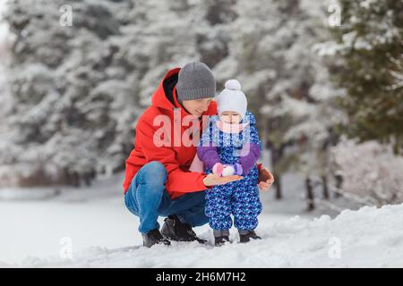 Petite fille souriante s'amusant avec son père dans un parc d'hiver.Mignon enfant de deux ans avec un parent jouant boule de neige maker jouet.Concept de famille heureuse et Banque D'Images