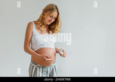 Femme blonde enceinte appliquant de la crème pour le ventre pour empêcher les marques d'étirement.Future mère tenant dans les mains tube avec lotion pour les soins de la peau. Banque D'Images