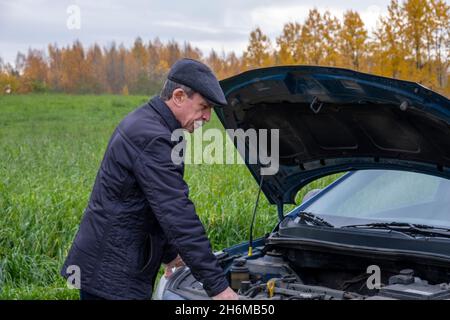 Un homme âgé à la retraite ouvre le capot de sa voiture et regarde dans le moteur Banque D'Images