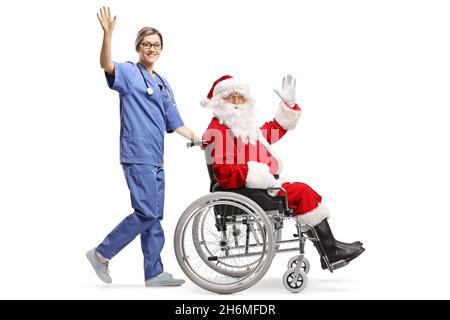 Prise de vue en profil d'une infirmière féminine poussant le père noël dans un fauteuil roulant et agitant isolée sur fond blanc Banque D'Images