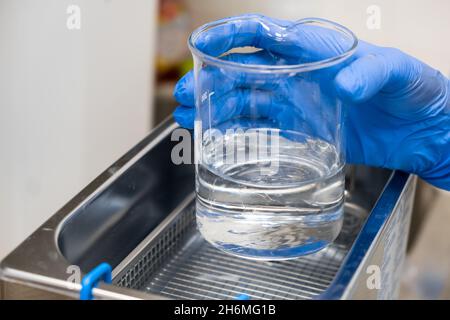 Le scientifique en caoutchouc bleu place un bécher pour dissoudre ou nettoyer dans un bain à ultrasons.Analyses cliniques, toxicologiques et médico-légales. Banque D'Images