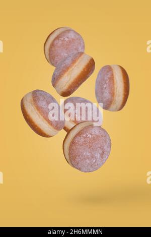 Beignets frais saupoudrés de sucre en poudre volant sur fond jaune.Dessert minimal et concept sucré Banque D'Images