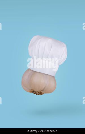 Ail frais avec chapeau de chef volant dans l'air isolé sur fond bleu.Concept d'ingrédient alimentaire sain.Concept de nourriture minimale. Banque D'Images