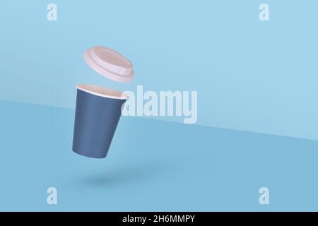 Une tasse à café jetable en papier avec capuchon blanc volant dans l'air isolé sur fond bleu.Concept de décollage minimal.Copier l'espace. Banque D'Images