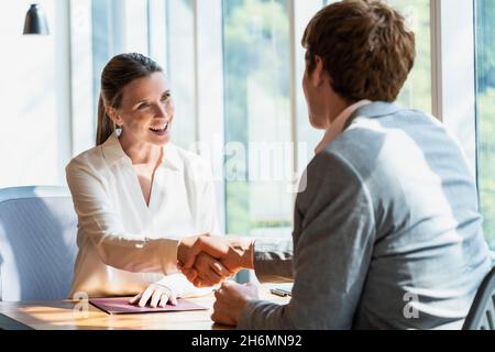 Femme mûre souriante se serrant la main avec un homme d'affaires au bureau Banque D'Images