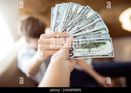 mère donne à son fils un paquet de dollars.Le client paie le travail en lui remettant de l'argent.Main tenant le compte-tours.Paiement par billets en espèces. Banque D'Images