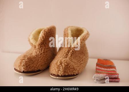 Pantoufles d'hiver chaudes en peau de mouton et chaussettes d'hiver sur sol blanc. Banque D'Images