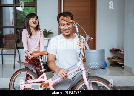 Sa fille rit avec joie lorsque son père termine l'assemblage de sa bicyclette Banque D'Images