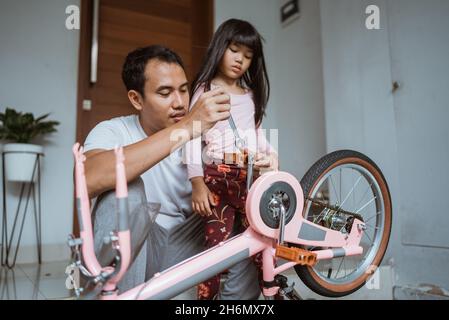 Père fixant une pédale de vélo avec sa fille Banque D'Images